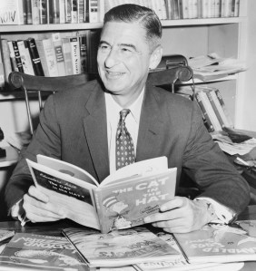 Ted Geisel (Dr. Seuss) half-length portrait, seated at desk covered with his books / World Telegram & Sun photo by Al Ravenna